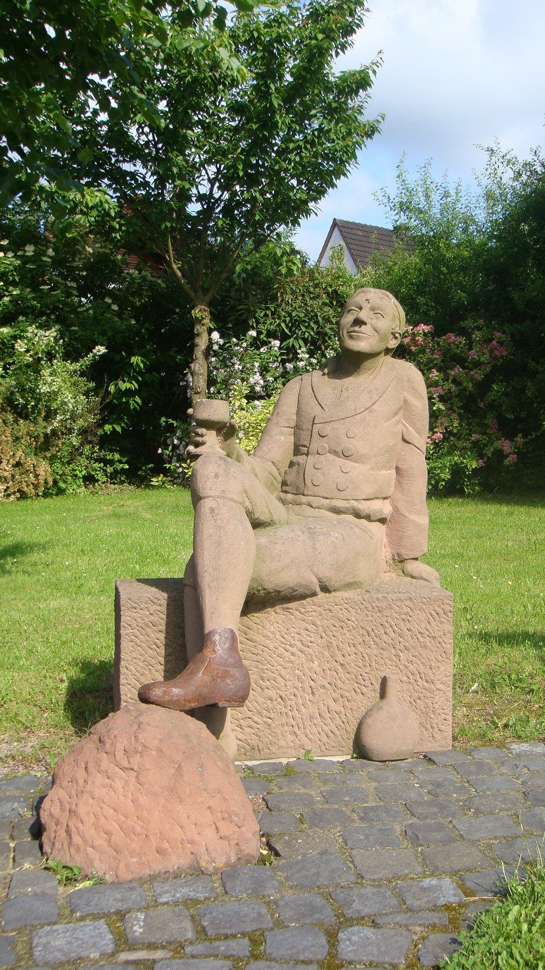 Sandsteinfigur, die verträumt sitzt und Wein trinkt.