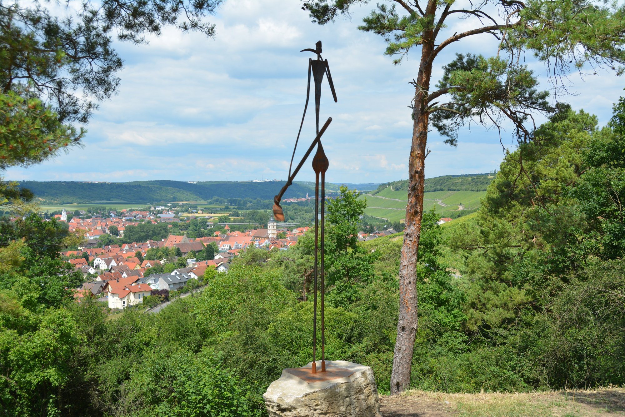 Es ist eine Skulptur von Arno Hey (Volkach) zu sehen. Sie ist aus Eisen gearbeitet und stellt eine Person dar, die einen Hacke in der Hand hat und auf den Main und die Weinberge schaut. 