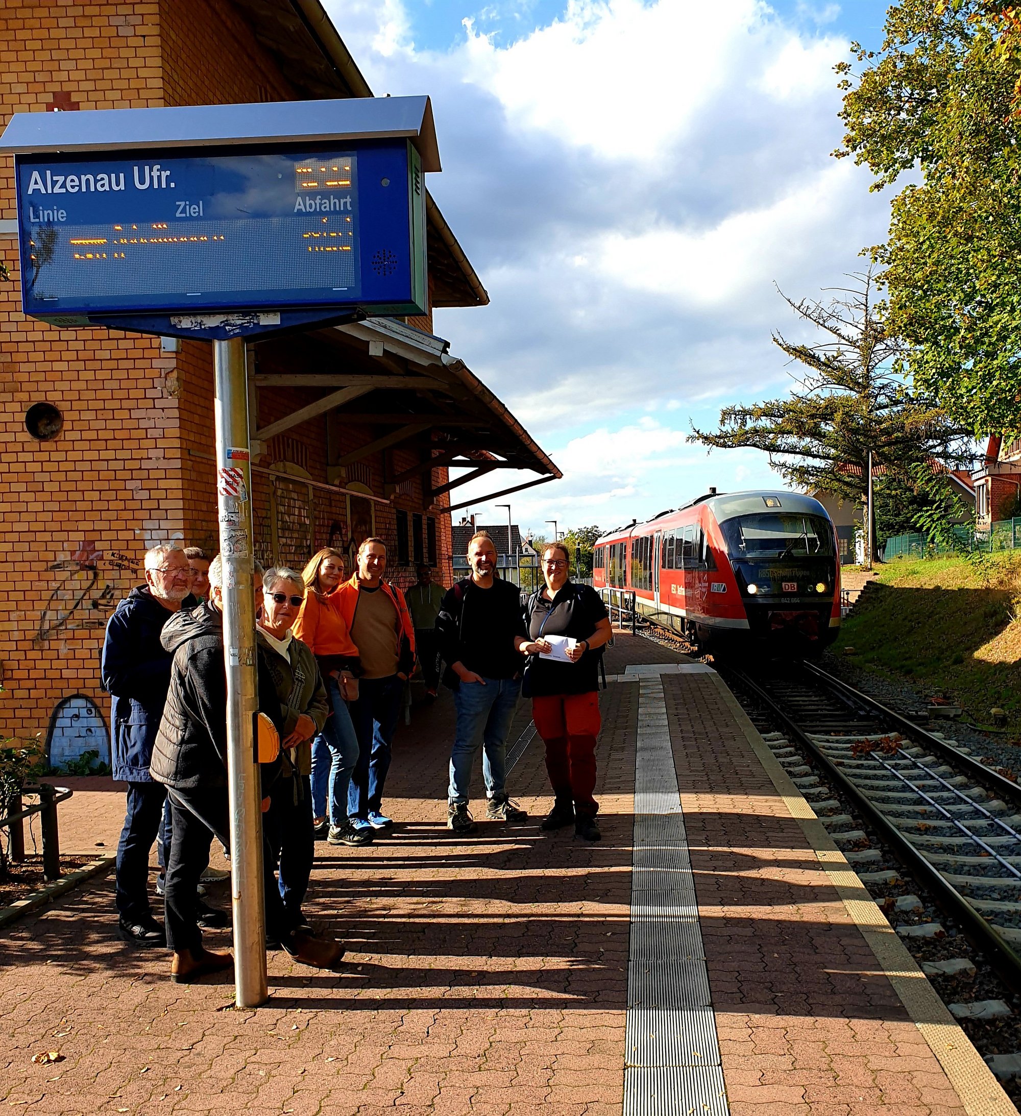 Personengruppe am Bahnhof mit einfahrender Bembel.