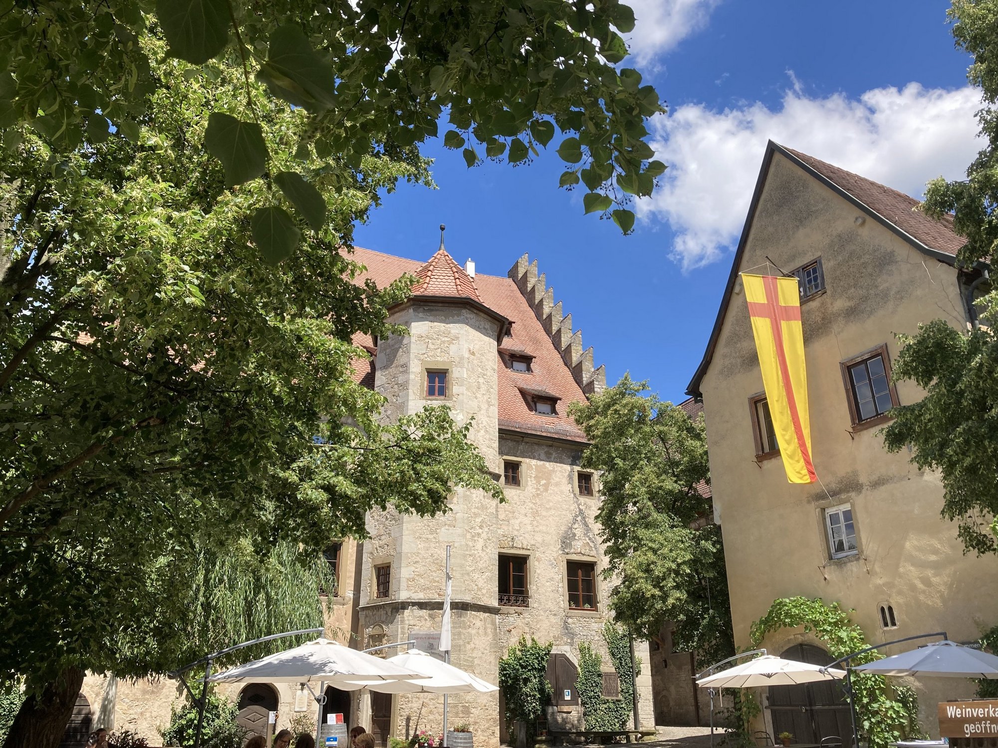 Auf dem Bild sind das Schloss Sommerhausen und der Schlosshof mit Sonnenschirmen, Stühlen und Tischen zu sehen.  